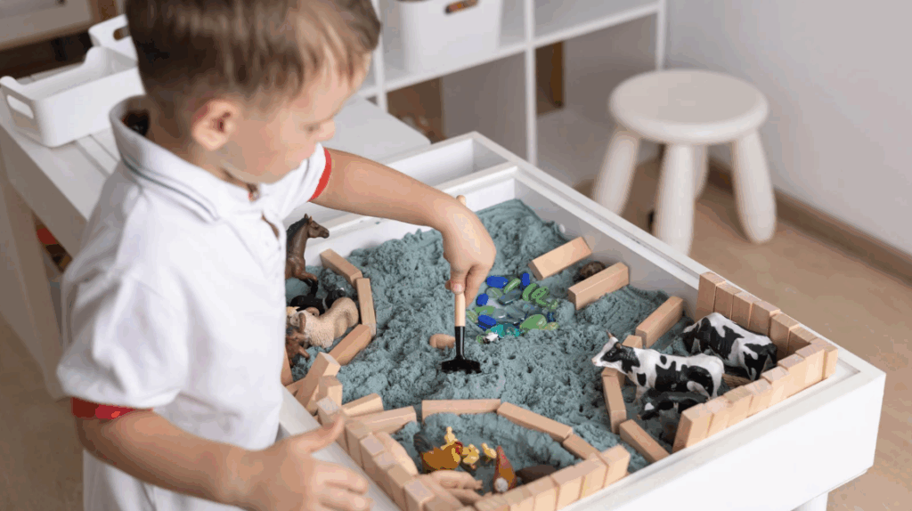 a baby boy exploring a sensory box with kinetic sand and farm animal toys